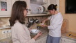 © Aliaksandr - Two sisters washing dishes together at a sunlit kitchen sink, passing plates and utensils, sharing household chores and bonding over everyday teamwork and domestic life