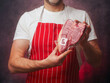 © mark_gusev - Masculine male butcher in white shirt and red and white classic stripe apron showing top quality T-bone steak in vacuum package for extra freshness of the product. Top price beef promotion.