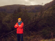 © mark_gusev - Energetic man in a red jacket stands in a forest with his arms crossed. He is wearing a yellow hat and sunglasses. Scene is calm and peaceful, as the man is surrounded by nature. Travel and tourism
