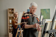 © Seventyfour - Senior Caucasian man painting on canvas in art classroom, focused on brushwork, senior Caucasian woman standing behind him painting, participating in educational art lesson