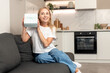 © brizmaker - Woman smiling, holding gift box and sitting on sofa at home