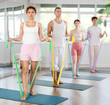 © JackF - Slim male and female attendees of pilates classes working out arms with band standing on mat in training room