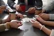 © New Africa - Team building. Group of businesspeople with takeaway cups solving puzzle together at dark wooden table indoors, closeup