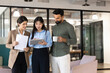 © fizkes - Diverse colleagues standing in coworking office, collaborating on task, reviewing project strategy using digital tablet, discussing business application, engaged in teamwork, communicate at workplace