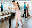© JackF - Expressive Hispanic guy in formal attire practicing sensual bachata with attractive young brunette in light flowing dress in dance class. Social dancing concept..