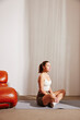 © Maskot - Active woman wearing sports clothes doing yoga while sitting on exercise mat at home