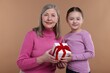 © New Africa - Little girl greeting her grandmother with gift on dark beige background