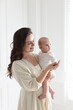© New Africa - Smiling mother in dress holding her cute baby near white wall at home