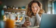 © NovaVision - Woman looking stressed while holding her phone and resting her head on her hand