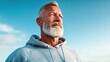 © NovaVision - An older man with a white beard looks up against a bright blue sky in a hopeful pose.