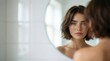 © Sergiy - A beautiful young woman with short brown hair, striking blue eyes, and natural freckles gazes intently at her reflection in a round mirror, symbolizing self-care and authentic beauty.