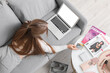 © Pixel-Shot - Young woman with laptop and credit cards shopping online on sofa at home, top view