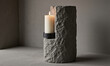 © panophotograph - Candle stone holder burning pillar candle sits on a rough hewn grey stone base against a minimalist concrete wall with copy space