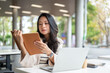 © bongkarn - Asian woman reading a book aside laptop and coffee cup while sitting at table in university building