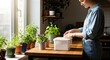 © Yurgentum - A woman in a denim shirt placing a lid on a container in a bright kitchen with lush potted plants.
