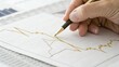 © nunoi - Hand holding a pen pointing at a fluctuating line graph on paper, analyzing financial data and trends.