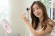 © Pormezz - women hairdo makeup routine, Young woman looking at the mirror and using iron hair curling curly long hair at home.