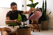 © kleberpicui - Adult man watering indoor plants in a cozy apartment living room, showing daily plant care routine, home wellbeing and sustainable urban lifestyle.