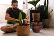 © kleberpicui - Adult man adjusting soil while repotting a houseplant indoors, representing plant maintenance, home gardening and sustainable lifestyle habits.