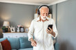 © Jelena Stanojkovic - Senior man, headphones and retirement for music, relax and positive mood on weekend with radio in house. One person, listening and happy in living room for podcast, streaming or jazz with happiness.