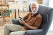 © Jelena Stanojkovic - Smile, relax and a senior man with a phone on the sofa for social media, contact or communication. Happy, online and an elderly person on the home armchair with a mobile for an app or typing a chat.