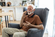 © Jelena Stanojkovic - Shot of an elderly man on a call using his cellphone on the sofa at home. Elderly guy enjoys online chatting, spends time in social networks, using phone and smiles.