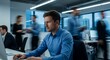 © Photo Verse - high quality, sharp focus, detailed, man sitting at desk, working on laptop, office setting with people in background, focused expression, blue shirt, professional