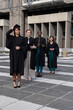 © wavebreak3 - Diverse female graduates posing on tiled campus plaza wearing black gowns and adjusting mortarboard