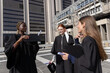 © wavebreak3 - Diverse female graduates in black gowns posing on tiled plaza, holding caps and rolled diplomas