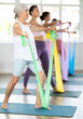 © JackF - Elderly woman doing pilates exercises with elastic band in group in fitness studio
