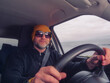 © mark_gusev - Male driver in his 40s or 50s in dark clothes and yellow hat and dark sun glasses. Man with grey beard behind driving wheel, happy friendly face Transport and tourism.