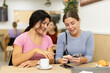 © JackF - Latin girl is chatting with female friend at table in cafe, showing photos on phone screen, sharing photo memories. Casual conversation, socializing with friends. Friendly atmosphere, coffee break.