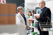 © DC Studio - Senior male and female individuals stand in drugstore, discussing medical products. Caucasian female pharmacist guides senior man in selecting suitable health supplements and wellness items.