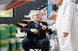 © DC Studio - Male customer listens to medical specialist during consultation in pharmacy, checking oxygen levels. Senior woman in lab coat assists wheelchair patient while explaining pharmaceutical products.