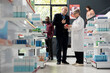 © DC Studio - Female pharmacist helps senior male customer choose appropriate medication in drugstore. Medical professional explains prescription details confidently while standing near organized pharmacy shelves.