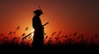 © Elzayady - Silhouette of a samurai warrior with a sword standing in tall grass at sunset with an orange sky
