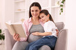 © New Africa - Pregnant woman and her daughter reading book together on armchair at home