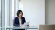 © Yuliia - Professional Asian businesswoman in navy suit reviewing documents at modern office desk near windows for corporate presentations and business meetings.