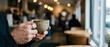 © Yuliia - Man holding coffee cup in modern cafe with warm lighting and blurred customers in background creating cozy atmosphere for relaxation and social gathering.