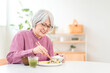 © buritora - A gray-haired senior woman eating in the dining room at home