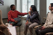 © pressmaster - Black young adult woman comforting Hispanic woman during support group session while Caucasian middle aged woman listening attentively in modern meeting room