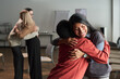 © pressmaster - Hispanic woman and Black woman embracing each other in group therapy session, smiling and showing support, with another pair of middle aged women hugging in background