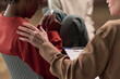 © pressmaster - Middle aged Caucasian woman comforting Black teenager sitting with knees up, teenager holding tissue and looking down, supportive gesture visible with hand on shoulder
