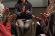 © pressmaster - Group of diverse adults sitting in circle clapping hands during support meeting, visible hands and partial faces showing multiethnic women participating in group activity