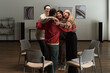 © pressmaster - Diverse group of adults standing in circle embracing each other in support group setting, smiling and connecting, empty chairs arranged around them, modern artwork on wall