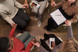 © pressmaster - Diverse group of middle aged and young adult women sitting in circle holding hands during support group session, visible brochures and clipboard suggesting mental health or counseling context