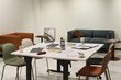 © pressmaster - Modern office workspace showing empty table with scattered documents, coffee cups, digital tablets, stationery and chairs, background featuring sofa seating and minimal decor
