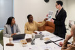© pressmaster - Multiethnic group of women discussing business strategy in modern office, one woman pointing at document while middle aged colleague presenting printed chart
