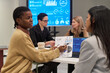 © pressmaster - Black young adult woman discussing business analytics with Hispanic young adult woman in office meeting, multiethnic group of young adult women collaborating on project, digital charts visible