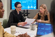 © pressmaster - Caucasian middle aged women discussing business documents at meeting table with charts and graphs on screen, diverse colleagues collaborating nearby